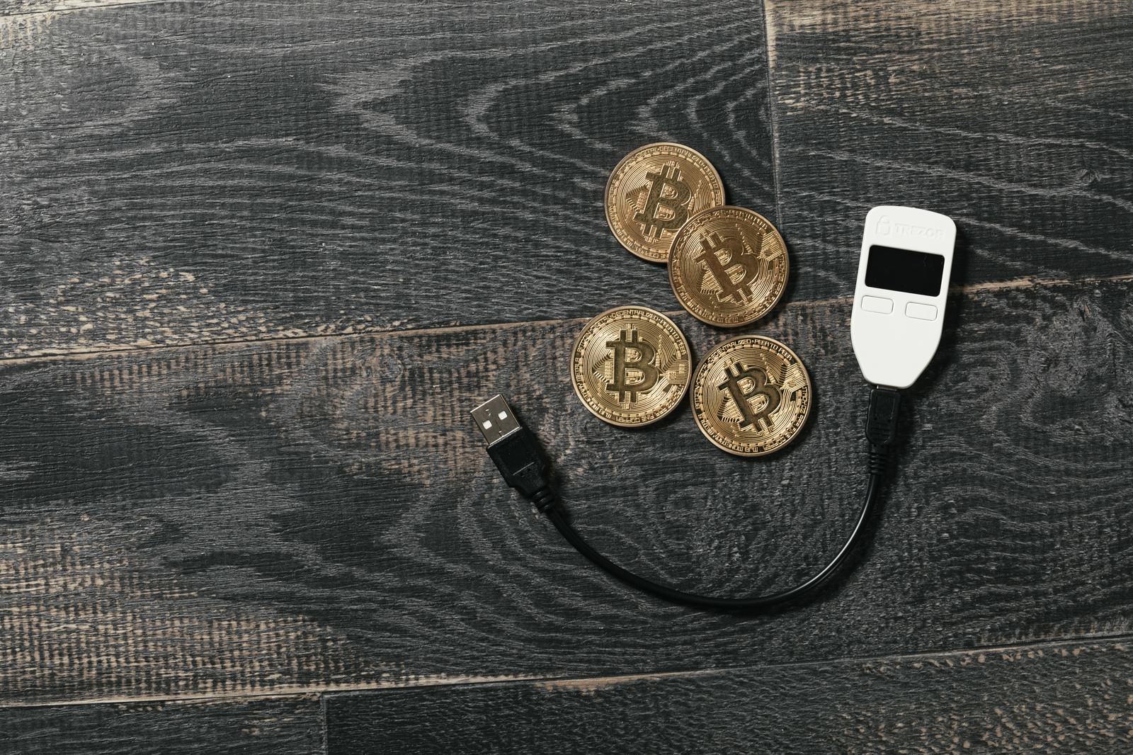 木目調の背景に置かれた金色のビットコインコインとTREZORハードウェアウォレット