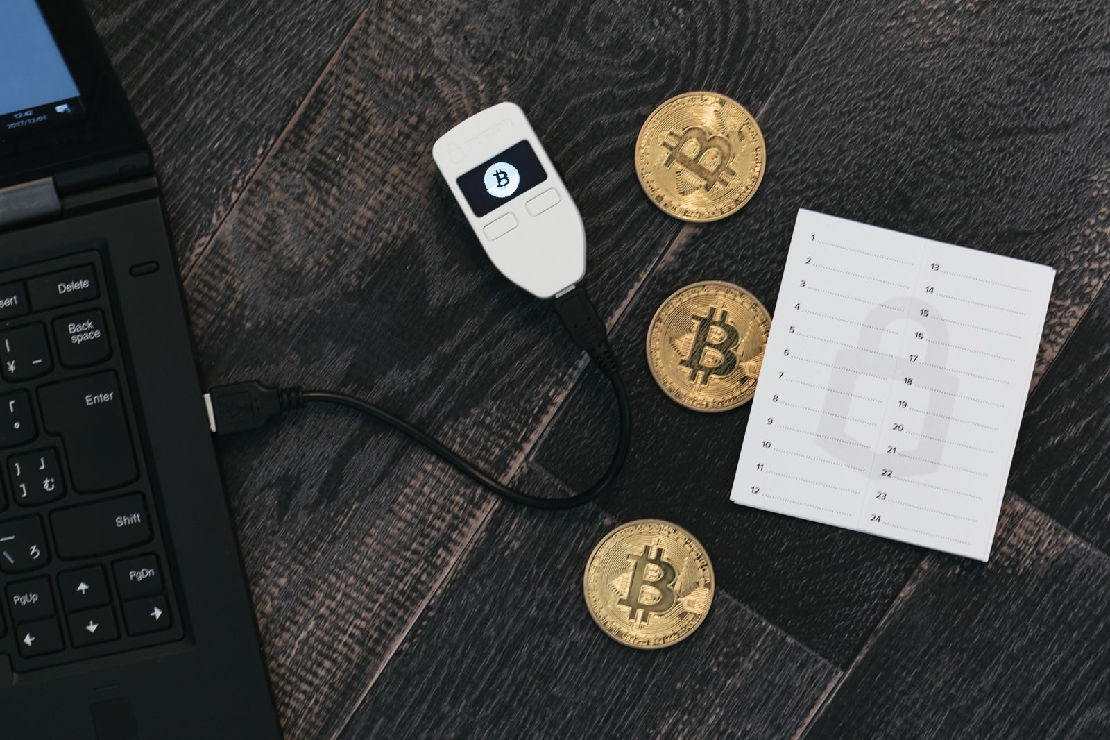 デスクに散らばる3枚の金色ビットコインとTREZORウォレット、投資グラフ