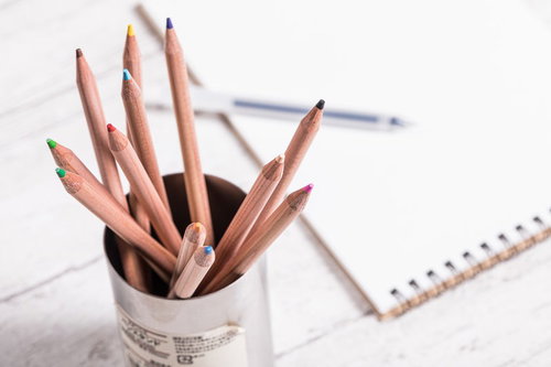 白いペン立てに立てられた色鉛筆と文具の机上風景