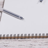 木目調のデスクに置かれた何も書かれていないメモ用紙とペンの写真