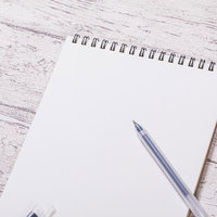 白紙のリング式メモ帳とシルバーのボールペンの写真