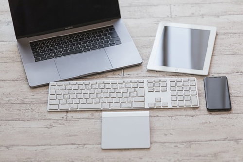 白いデスクに配置されたキーボード、スマホ、タブレットなどのガジェット