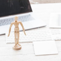 デスクの上に立つ木製デッサン人形とノートパソコン、付箋やメモの写真