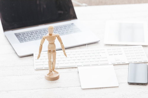 デスクの上に立つ木製デッサン人形とノートパソコン、付箋やメモ