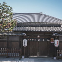 伊予食堂おとらの薬医門と瓦屋根の門構え、白い塀と提灯の写真