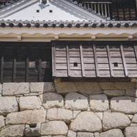 石垣に伸びる塀の影と白漆喰の城郭建築－松山城の写真
