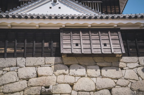 石垣に伸びる塀の影と白漆喰の城郭建築－松山城