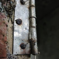 錆び付いた丁番と木製枠の劣化した金属ハードウェアの写真