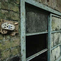 朽ちた壁に取り付けられたコンセントと廃屋の窓枠の写真