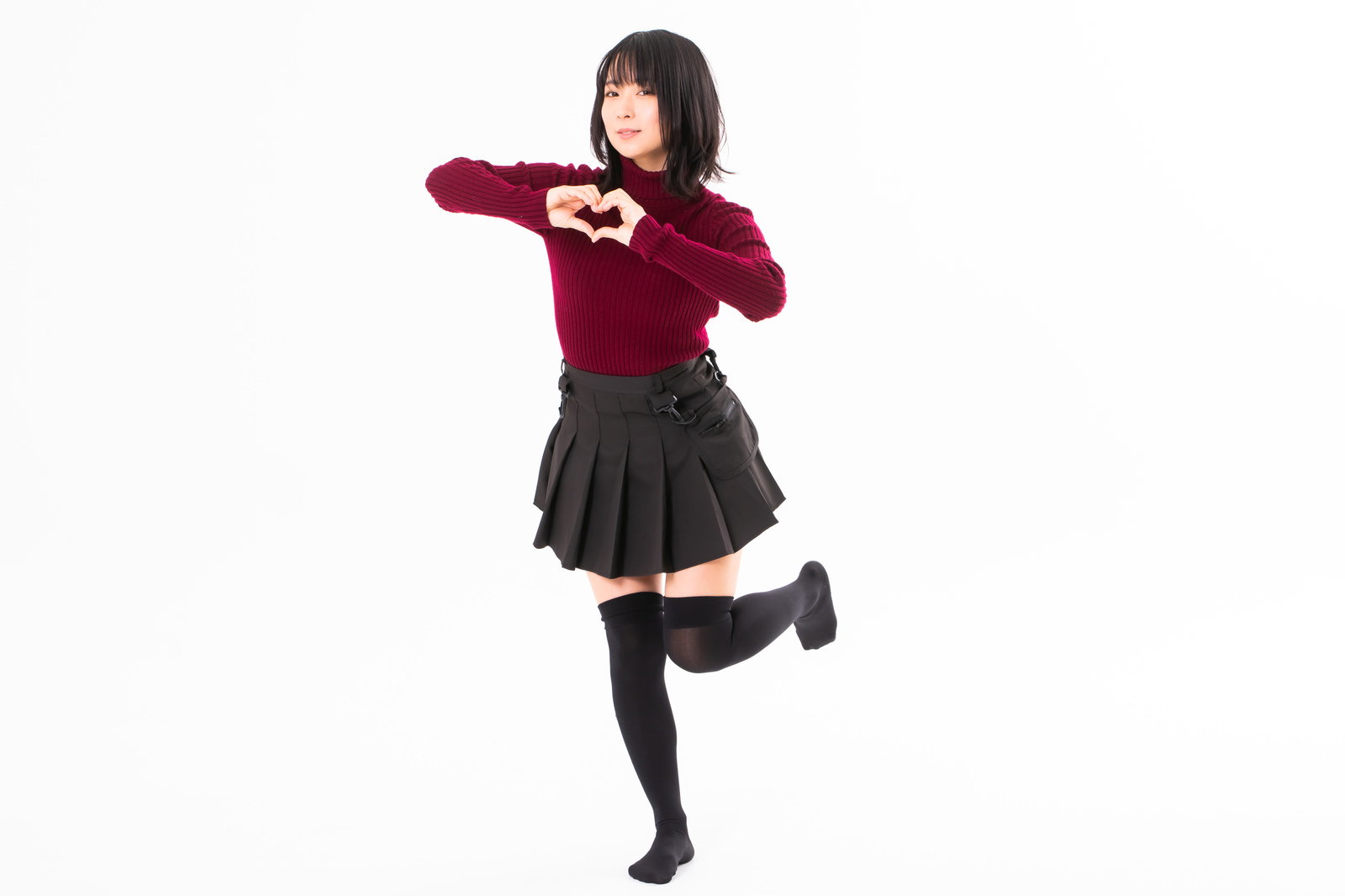 赤いセーターを着た女性が両手でハートマークを作っている［モデル：にゃるる］
