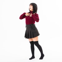 赤紫のニット、プリーツスカート姿で大きく胸を張る女性モデルの写真