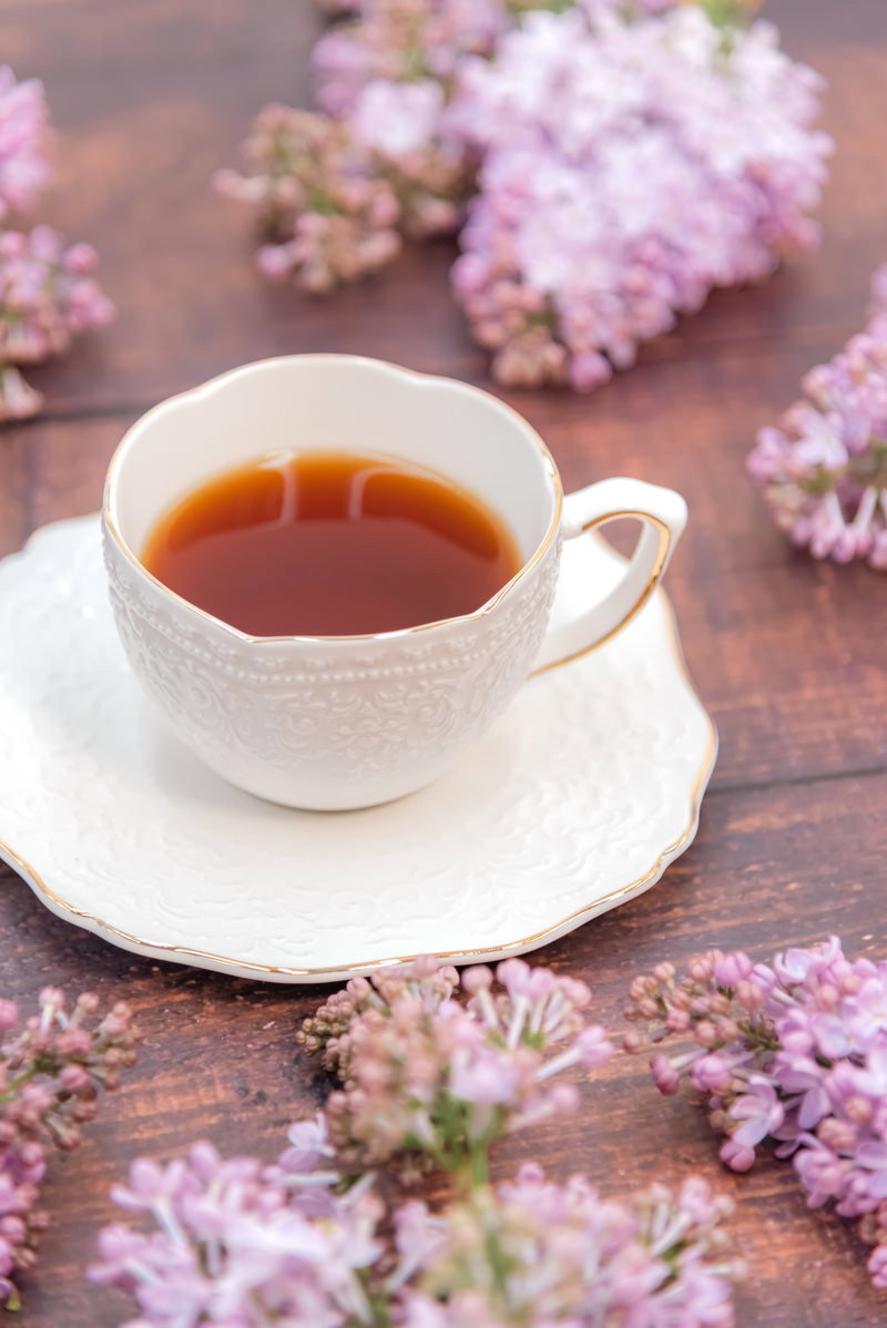 白いティーカップに入った紅茶と薄紫色のライラックの花が配置されたおしゃれな写真