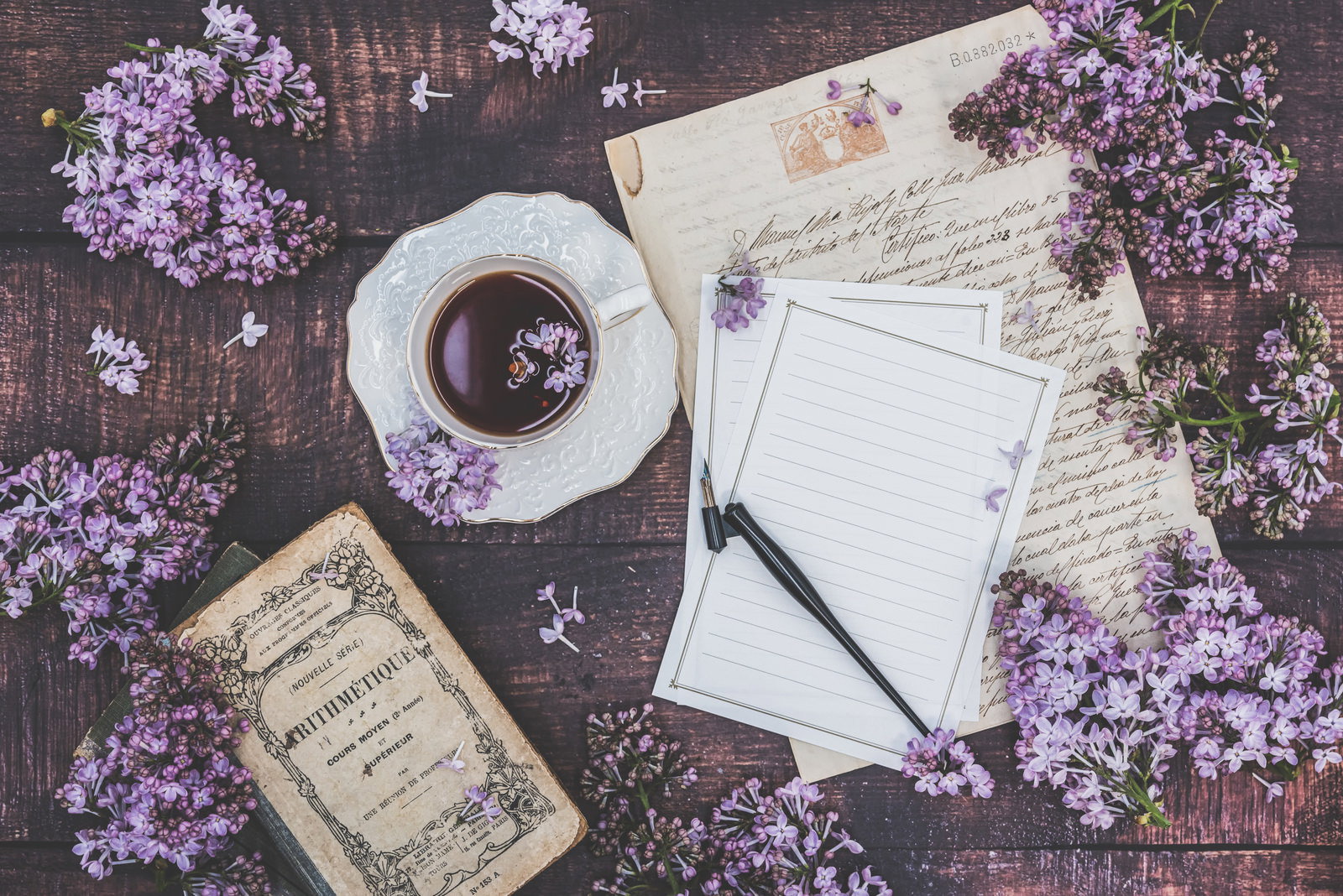 ライラックの花に囲まれた机の上のコーヒーカップと手紙