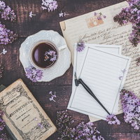 デスクに散らばるライラックとレターセット、コーヒーカップの写真
