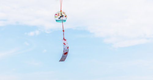 赤い紐に揺れる花柄の風鈴、空に舞う夏の音色