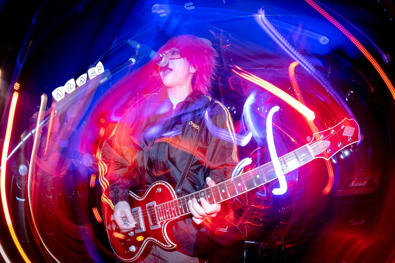 赤いライトアップの中でギターを演奏しながら熱唱する男性ギタリスト［モデル：のせさん］