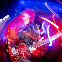 赤いライトに照らされて熱唱するギタリストの写真