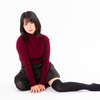 ボルドー色のニットを着て横座りしながら片足だけ伸ばす女性の写真