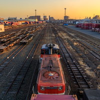 貨物ターミナルの朝焼けと赤い貨物列車が並ぶ複数線路の写真