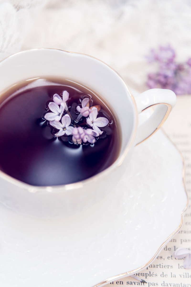 白いティーカップに注がれた紅茶の水面に薄紫色のライラックの花弁が浮かんでいる