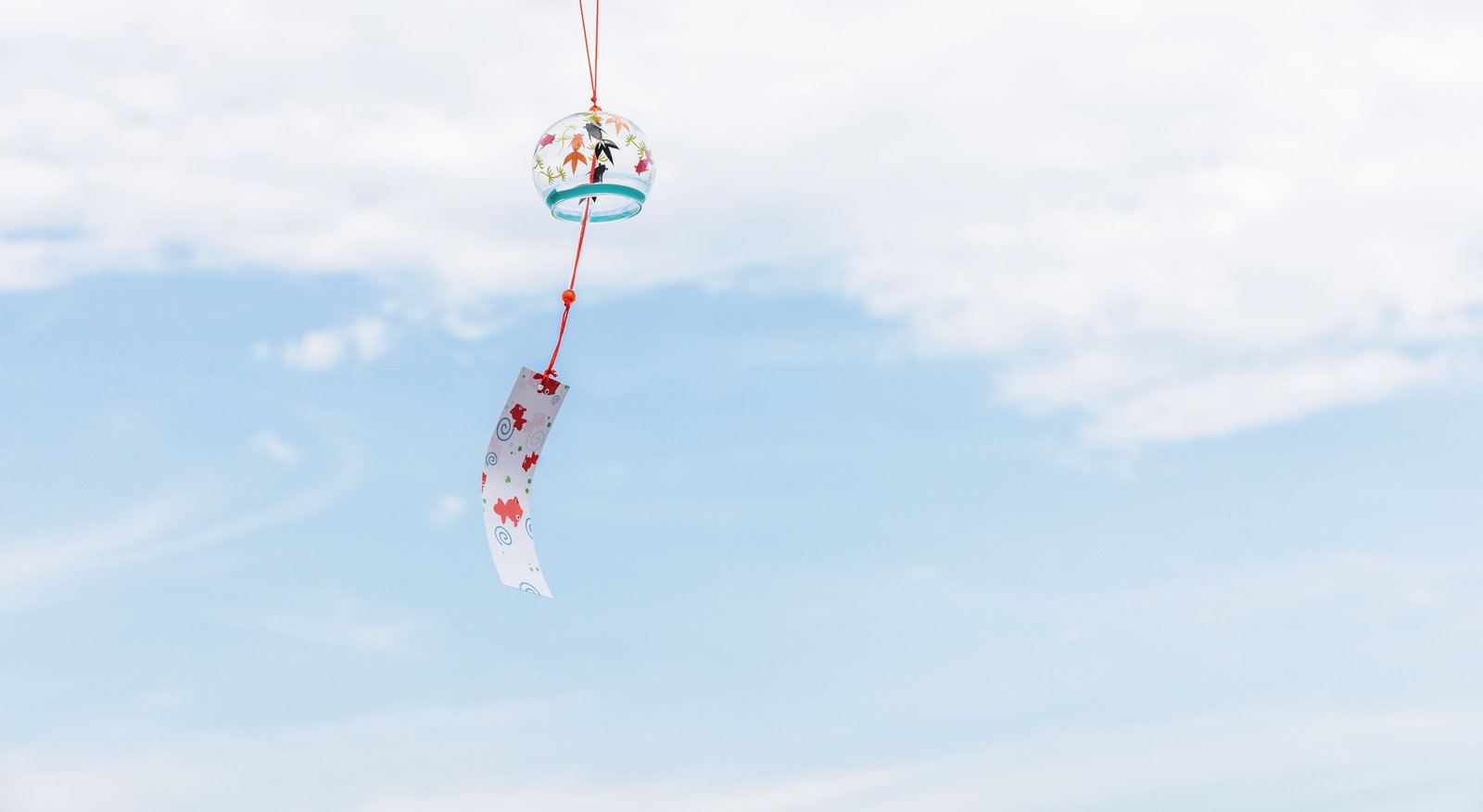 青空に揺れる赤い紐の風鈴と短冊