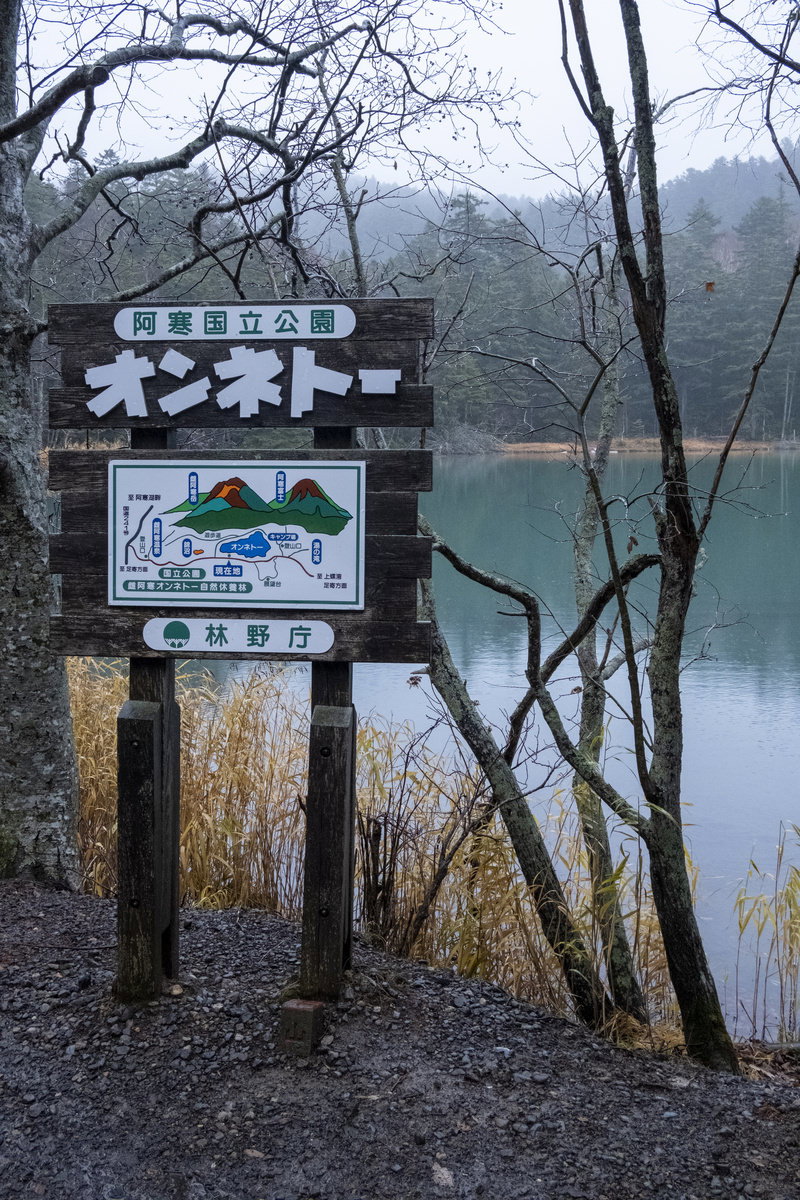 湖畔に立つ阿寒国立公園オンネトーの案内看板と背景の湖
