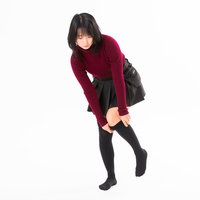 赤いワンピースを着て立ちながら黒いハイソックスを引き上げる女性の写真