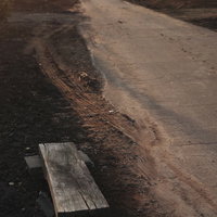 陽光に照らされる未舗装の農道とタイヤ跡、道端の休憩用の椅子の写真