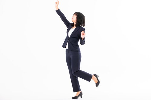 高い所に手を伸ばす紺色スーツの女性社員がファイルを取る