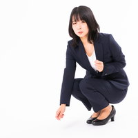 しゃがみ込んで落とし物に手を伸ばす黒スーツの女性の写真