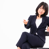 椅子に座ってざっくばらんに話し出す紺色スーツの女性社員の写真