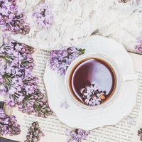 レースと洋書が添えられたライラック咲くハーブティーの写真