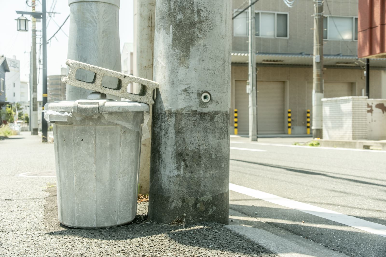 道路脇に設置されたコンクリートブロックと円筒形のゴミ箱