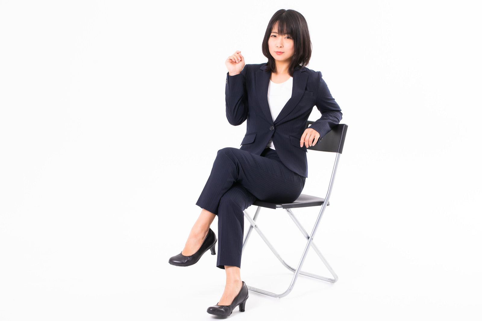 椅子に腰掛けて足を組みポーズをとる黒いスーツ姿の女性［モデル：にゃるる］