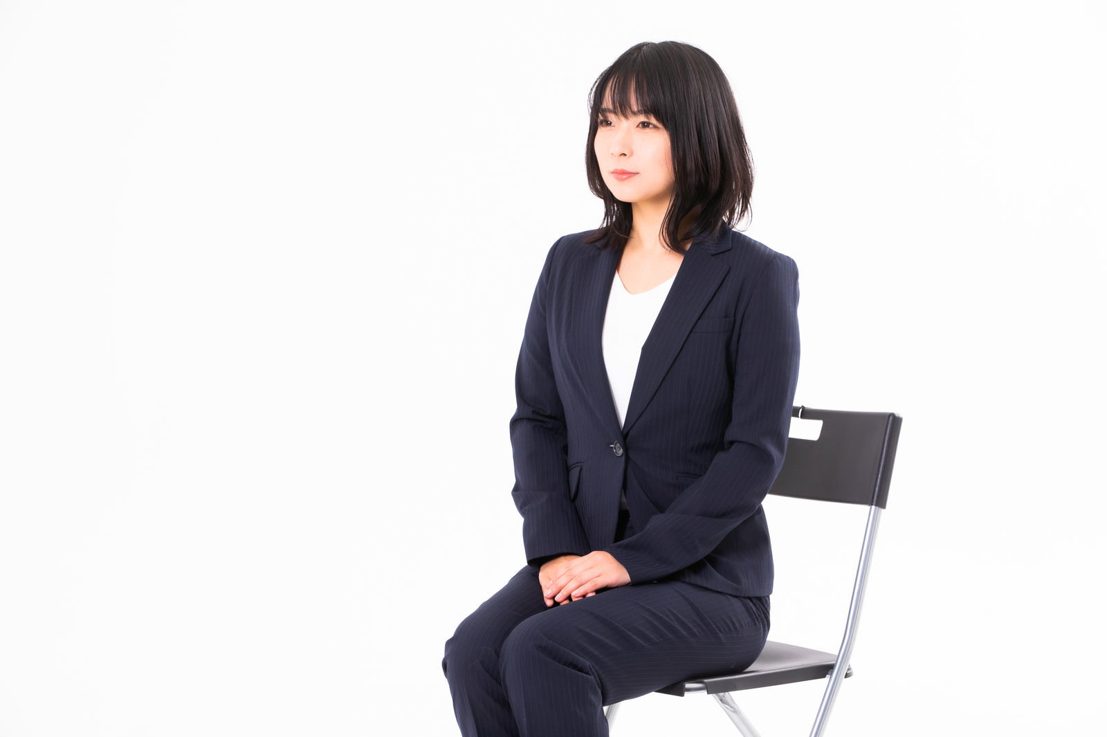 椅子に座って笑顔で話を聞く紺色のリクルートスーツ姿の女性［モデル：にゃるる］