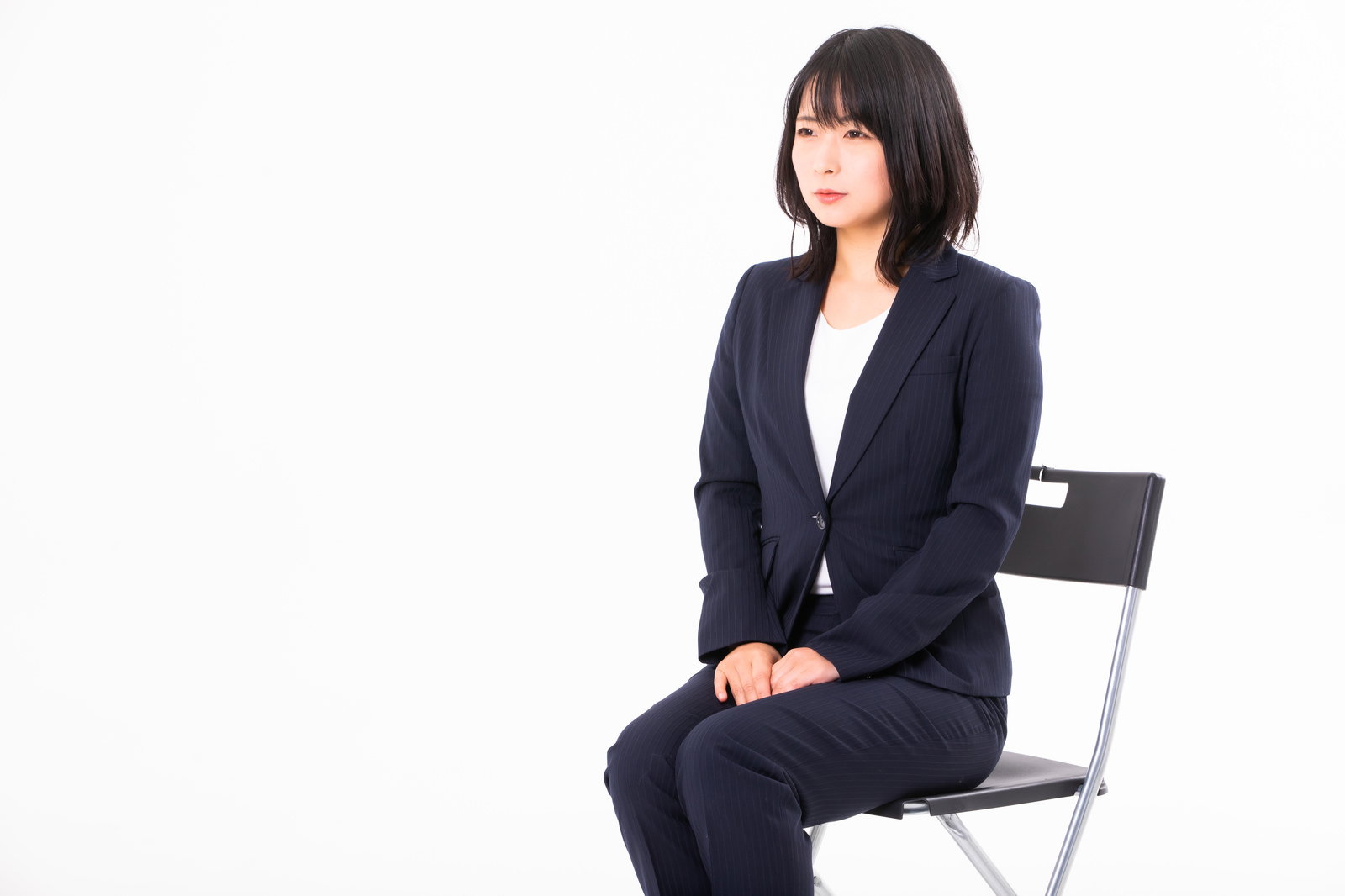 紺色のスーツを着て白い椅子に座る女性［モデル：にゃるる］