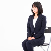面接中に白い椅子に浅く座る紺色スーツの女性社員の写真