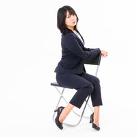 椅子に腰掛けてひと休みする紺色スーツの女性社員の写真