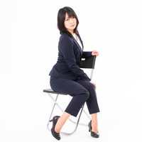 白い椅子に腰かけてこちらを見つめる女性社員の写真