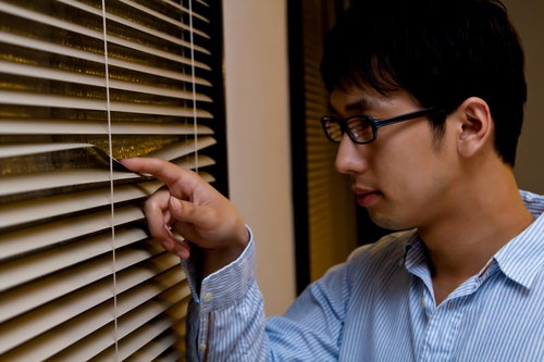 暗い室内でブラインドの隙間から外を覗く男性