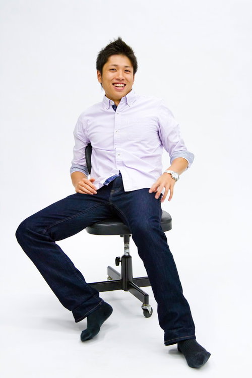 白い背景の前で椅子に座って笑顔を見せる男性