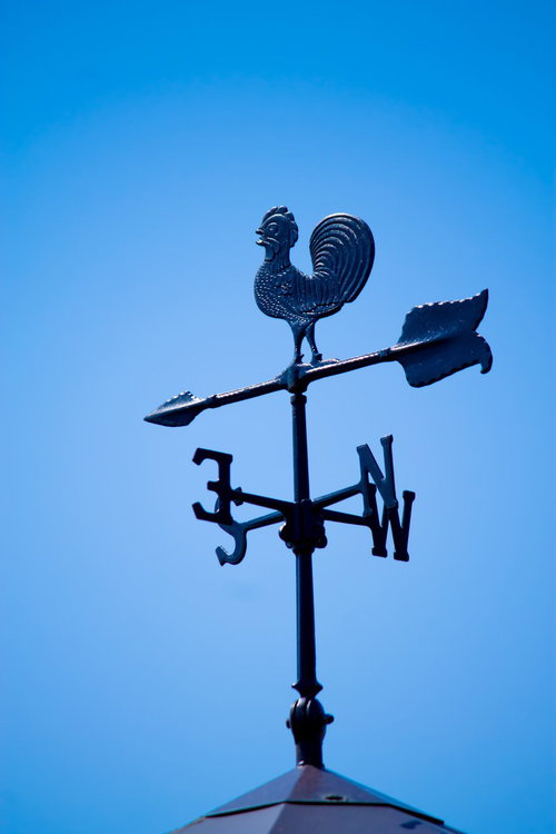 青空を背景に屋根の上に立つ金色の風見鶏