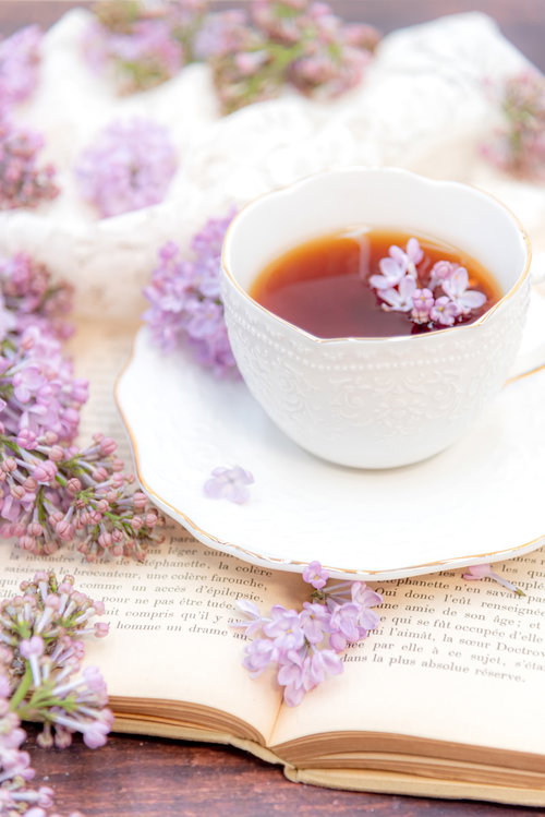 散りばむライラックと洋書の上に置かれたハーブティー