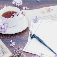 白紙の手紙と散らばるライラック、ティーカップと万年筆の写真