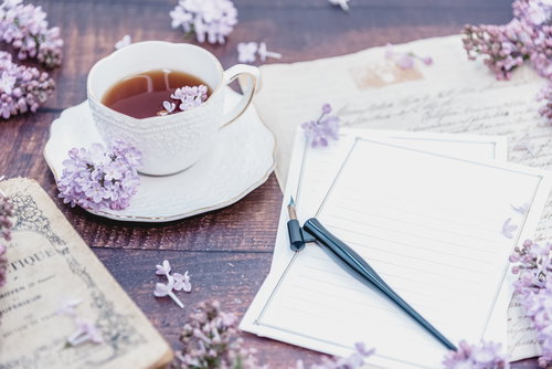 白紙の手紙と散らばるライラック、ティーカップと万年筆