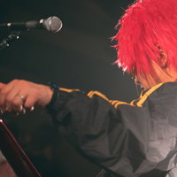 ステージでギターをチューニングするギタリストの背後姿の写真