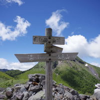 日光白根山の山頂に立つ木製指導標と青空の写真