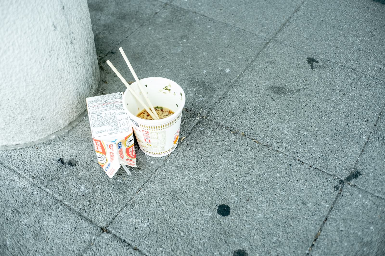 コンクリートの地面に箸と一緒に放置された食べかけのカップ麺
