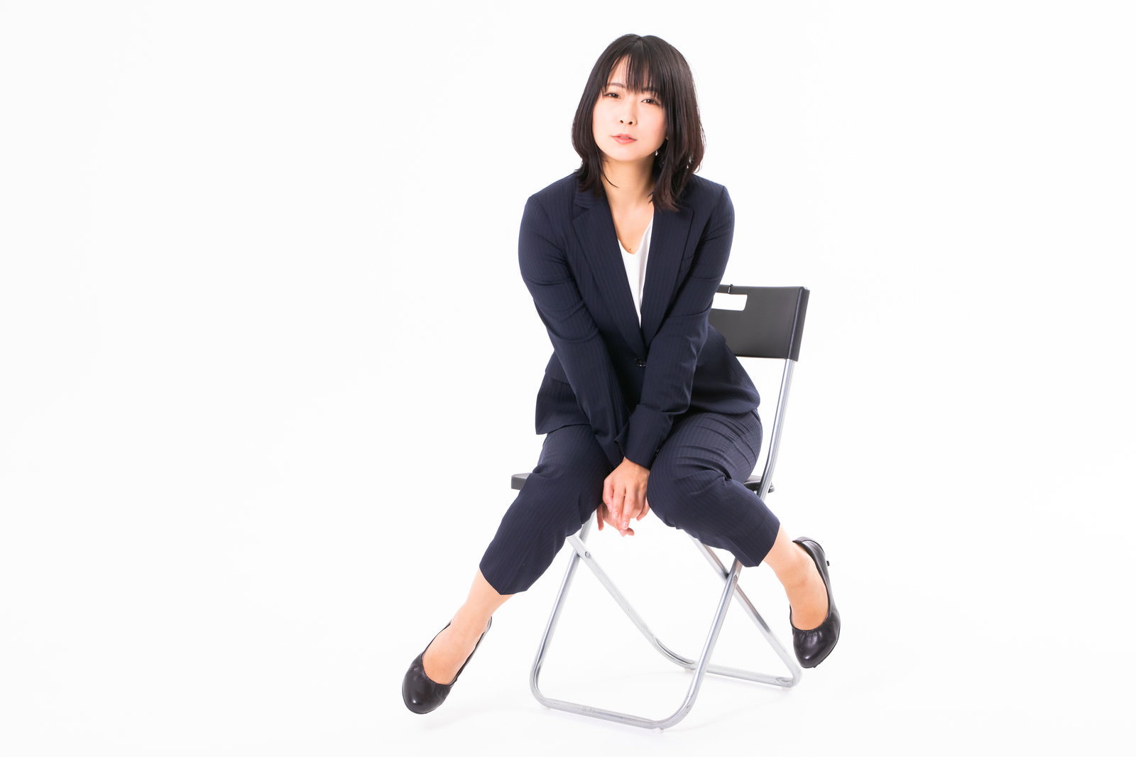 紺色のスーツを着た女性が白い椅子に座って休憩している様子［モデル：にゃるる］