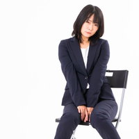 紺色のスーツを着てもじもじする女性社員が椅子に座るの写真